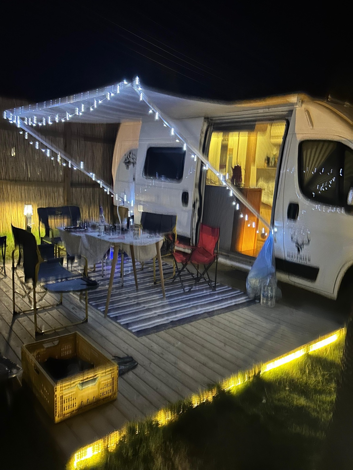 Gece ışıklarla aydınlatılmış karavan ve açık hava oturma alanı